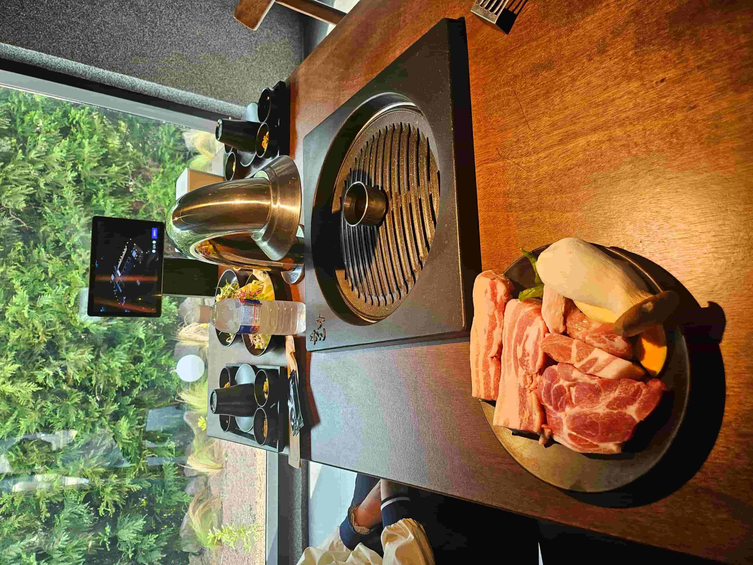 답례품 준비 전 체크리스트 관련 이미지 - 창밖 풍경을 즐기며 신선한 고기와 채소를 불판에 구워 먹기 전 준비된 식탁 모습입니다. 다양한 밑반찬과 함께 즐거운 식사를 시작할 수 있습니다.