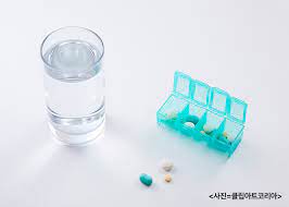 놀이 및 학습용품 관련 이미지 - 물 한 잔과 알약 정리함, 그리고 몇 개의 알약이 놓여 있어 약 복용을 준비하는 모습을 보여줍니다. 규칙적인 약 복용과 건강 관리에 활용하기 좋은 이미지입니다.
